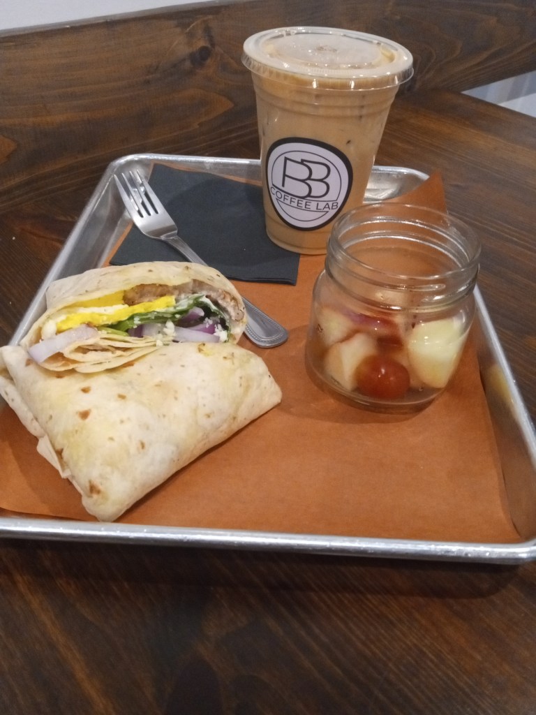 Breakfast burrito, iced coffee, and jar of fruit on a metal tray