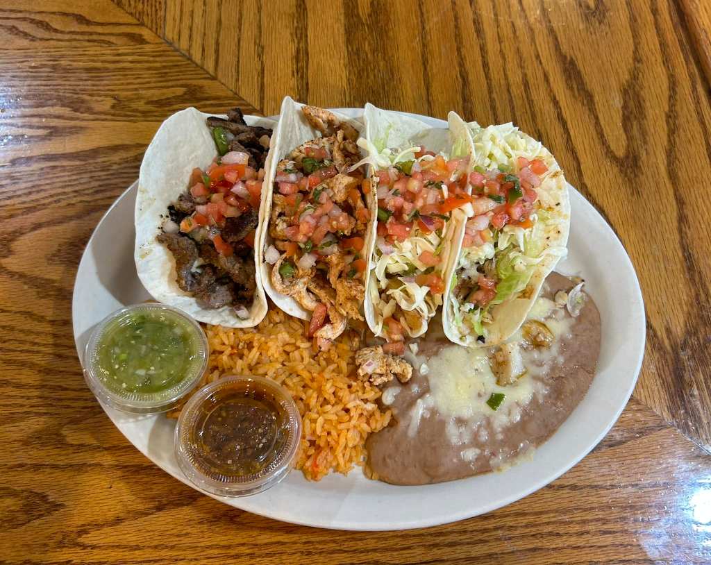 Four soft shell tacos on a plate with rice and refried beans.