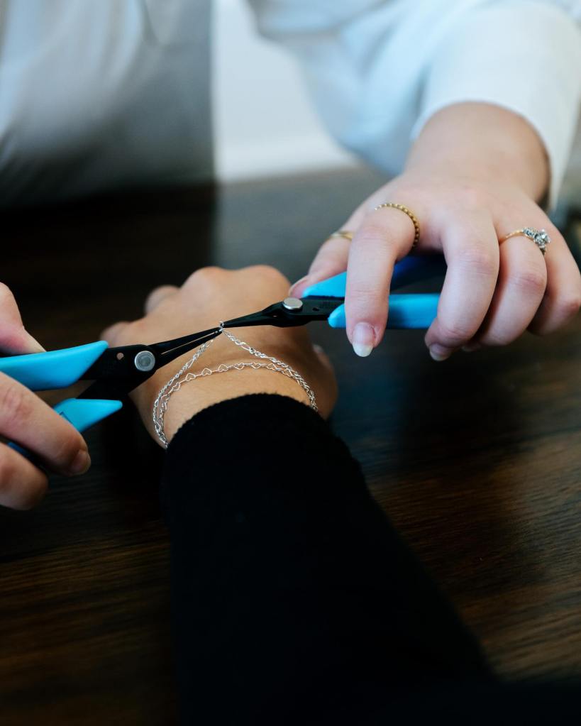 A jewelry maker using pliers to attach a jump ring on a permanent bracelet on someone's wrist