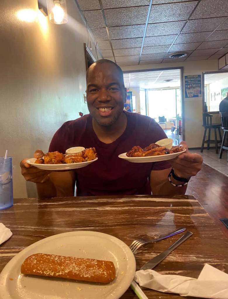 Food influencer KG sitting at a table holding a plate of chicken wings in each hand
