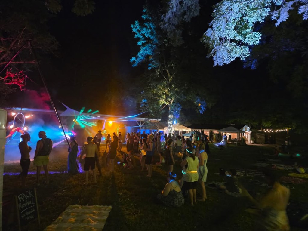 An outdoor music performance at night with lights and lasers and crowd of people in attendance.
